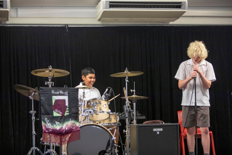 A band of students playing music. One is singing and the other playing the drums.